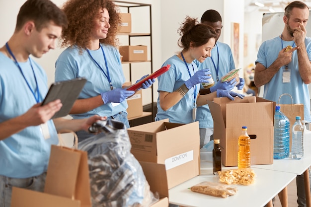 Foto diverse persone in guanti protettivi che smistano alimenti per imballaggio in scatole di cartone