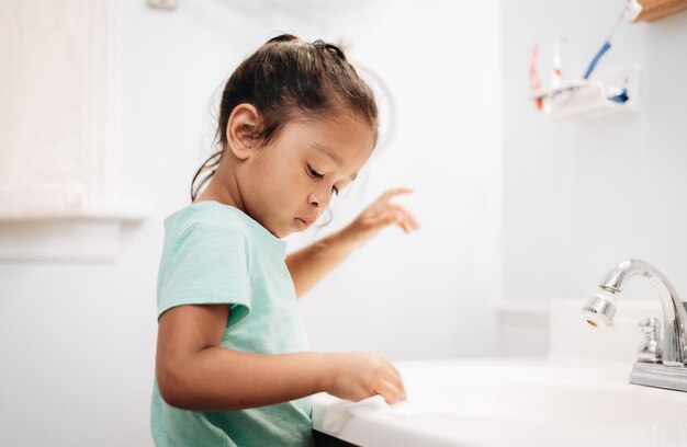 Photo diverse preschool girl at home in bathroom cleaning sink and washing hands chores and hygiene