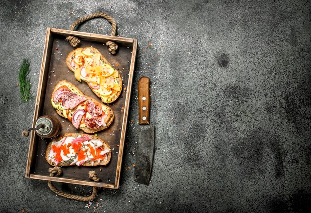 Diverse sandwiches met zeevruchten, vlees en groenten op een oud dienblad.