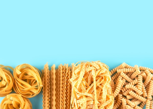 Diverse soorten pasta behang. Mix macaroni, spaghetti op blauwe achtergrond met kopie ruimte
