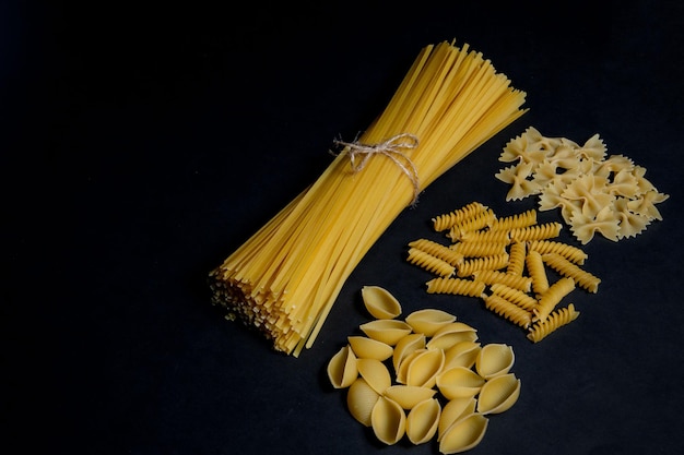Diverse soorten pasta op zwarte achtergrond. Bovenaanzicht. Verschillende vormen van pasta. Kopieer ruimte voor ontwerp.
