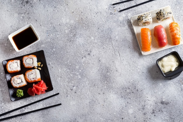 Diverse sushi die op zwart-witte plaat met stokken, saus op lichte steenachtergrond worden geplaatst