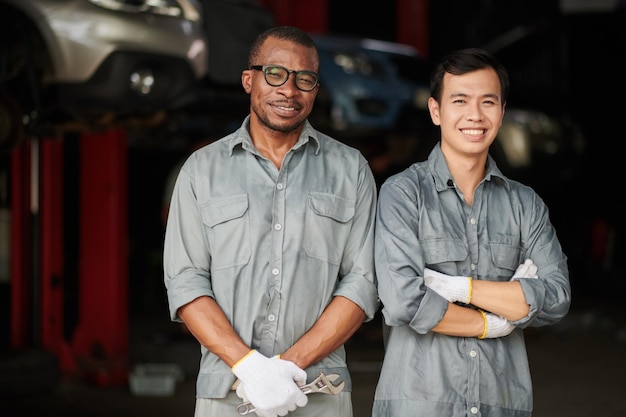 Diverse team of car mechanics in grey overalls standing in garage