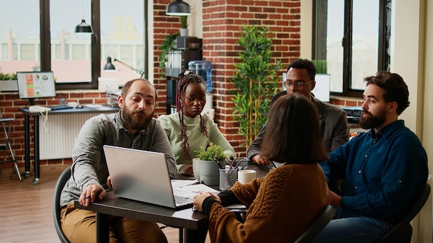 Diverse team of coworkers analyzing research data on laptop,\
planning business report and charts presentation in boardroom\
meeting. doing teamwork to create partnership project.