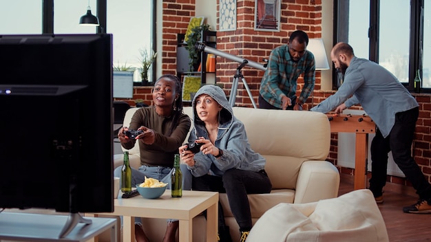 Diverse team of women playing video games on tv console, having\
fun with game play at home. cheerful people enjoying online gaming\
competition and challenge at friends hangout.