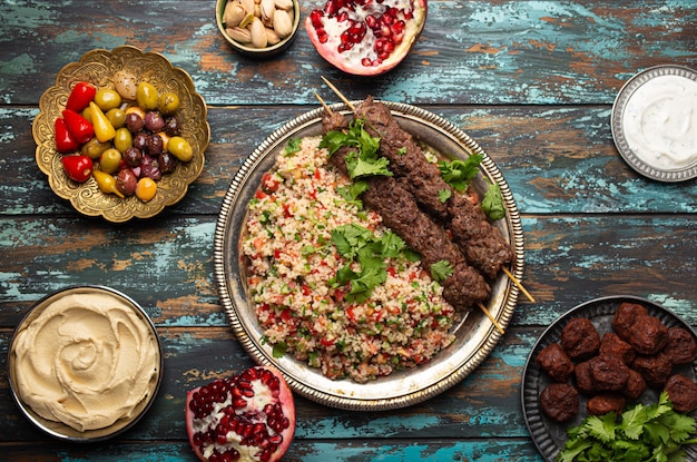 Diverse Turkse gerechten: vleeskebab met taboulehsalade, falafel, hummus, olijven, pistachenoten en andere Midden-Oosterse meze op houten tafelblad. Etnisch Arabisch eten, keuken van Turkije