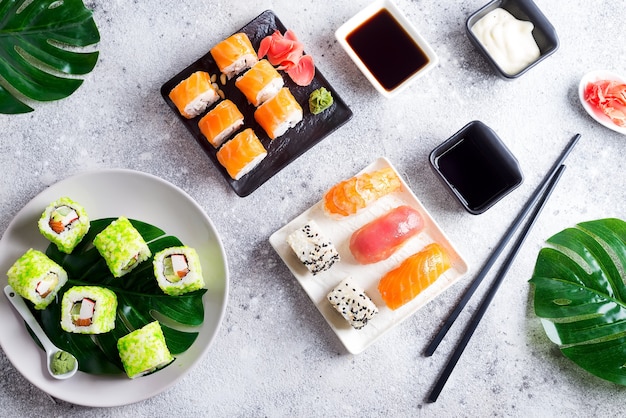 Diverse verse en heerlijke sushi die op zwart-witte leisteen met metaal en leisteenstokken, saus en groene bladeren op lichte steen worden geplaatst