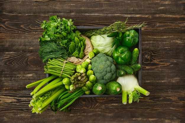 Diverse verse groene groenten in houten kist op houtoppervlak