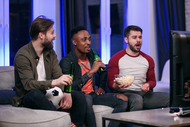 Diverse voetbalfans die voor favoriet team toejuichen en thuis bier drinken, exemplaarruimte