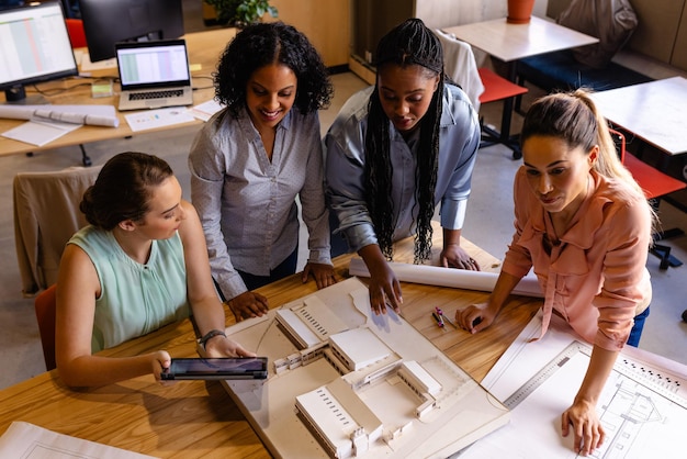 Foto diverse vrouwelijke architecten in discussie met behulp van modellen, blauwdrukken en tablet in casual office meeting. casual office, teamwork, business, lifestyle, design, communicatie en werk, ongewijzigd.