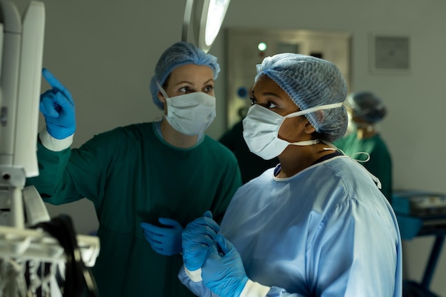 Diverse vrouwelijke chirurgen in discussie, die tijdens operatie medische apparatuur gebruiken in de operatiekamer. Ziekenhuis-, medische en gezondheidszorgdiensten.