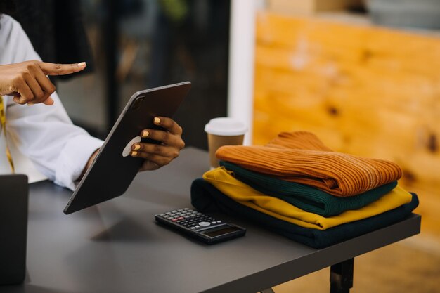 Diverse vrouwelijke modeontwerpers aan het werk met kleermaker centimeters op nek en houdt tablet en smartphone onafhankelijk creatief ontwerpbedrijf in studio