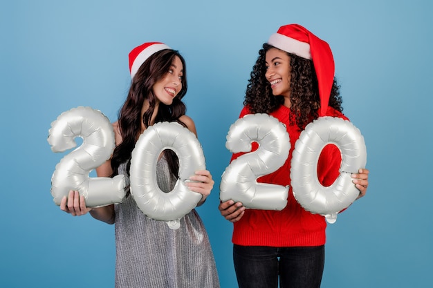 Diverse vrouwen met 2020 nieuwe jaarballons die geïsoleerde Kerstmishoeden dragen