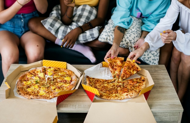 Разнообразные женщины сидят на диване, едят пиццу вместе