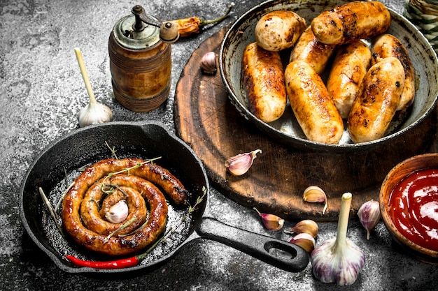 Foto diverse worstjes in pannen met knoflook en kruiden op een rustieke achtergrond