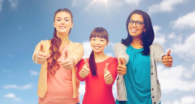 diversiteit, etniciteit en mensenconcept - internationale groep gelukkige lachende verschillende vrouwen die duimen omhoog laten zien over de blauwe lucht en de wolkenachtergrond