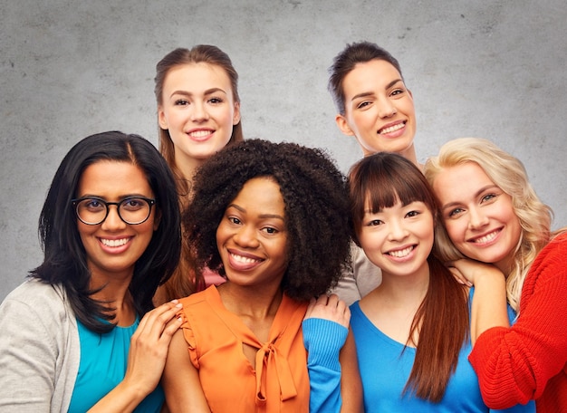 Diversity, ethnicity and people concept - international group of happy smiling different women hugging over gray concrete wall background