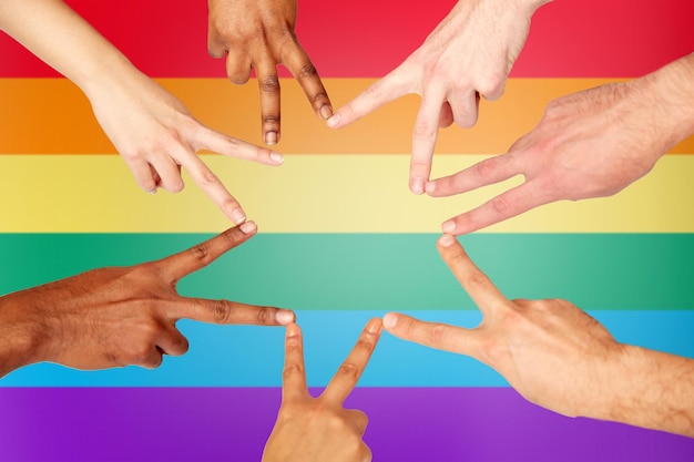 diversity, gay pride, tolerance, international and people concept - group of hands showing peace hand sign over rainbow background