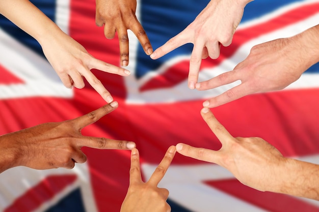 Foto concetto di diversità, immigrazione, etnia, internazionale e persone - gruppo di mani che mostrano il segno della mano di pace sullo sfondo della bandiera britannica