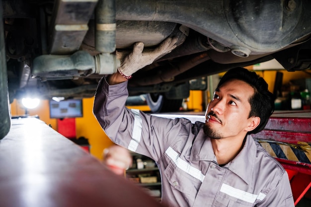 日本のメカニクがグレーのユニフォームを着て車の下部を検査する