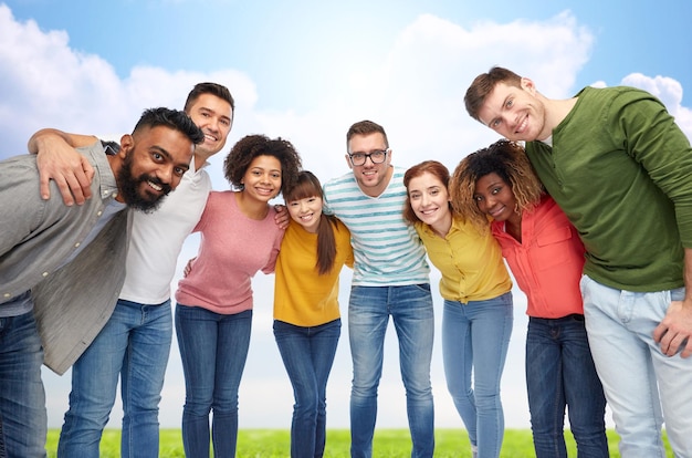 diversity, race, ethnicity and people concept - international group of happy smiling men and women hugging over blue sky background