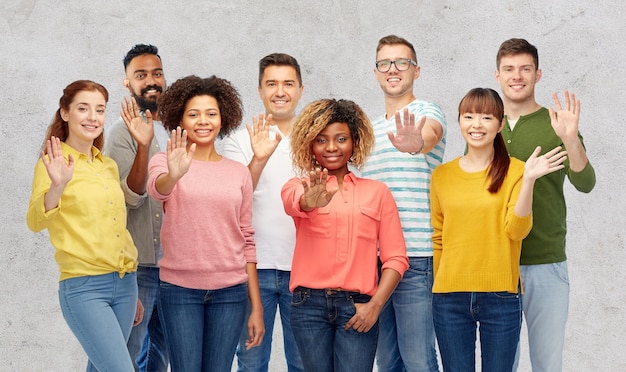 Foto concetto di diversità, razza, etnia e persone - gruppo internazionale di uomini e donne sorridenti felici che agitano la mano su sfondo grigio cemento