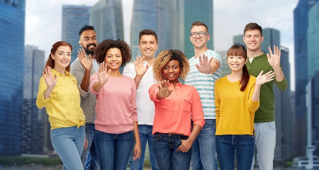 Diversity, race, ethnicity and people concept - international group of happy smiling men and women waving hand over singapore city skyscrapers background