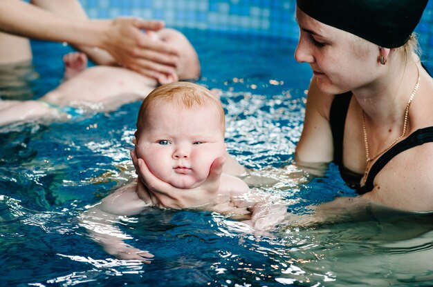 Diving baby in the paddling pool. Young mother, swimming instructor and happy little girl in pool. Learn infant child to swim. Enjoy the first day of swimming in water. Mother holding baby and dive