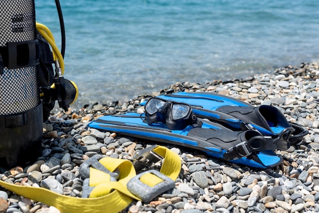 Diving equipment including oxygen tank fins goggles regulator weights on the shore of a rocky beach