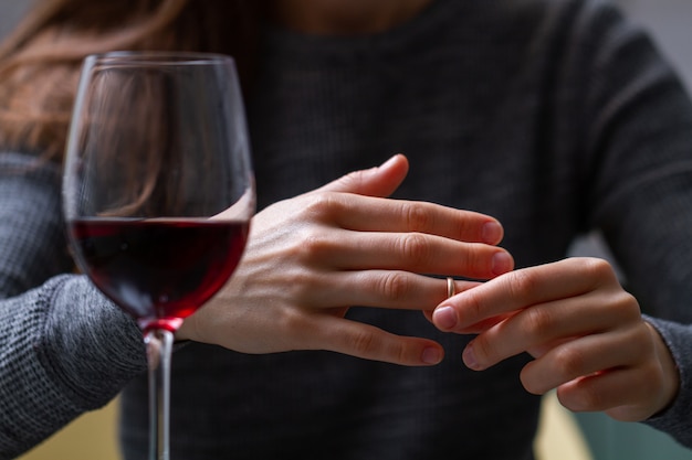 Divorced woman pulling wedding ring from finger and drinking a glass of a red wine because of adultery, betrayal and a failed marriage. Divorce concept. Relationship and love end. Life problems 