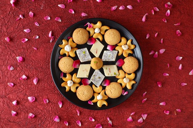 Diwali Diya on red background, Sweets OR Mithai in indian thali  arranged over decorative background