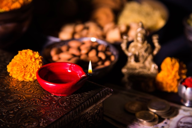 Diwali e preparazione per laxmi o lakshmi pooja con elementi come diya, banconote, dolci, fiori, snack, haldi e kumkum