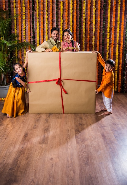 Diwali or Rakshabandhan Celebration - Indian young family of four celebrating Deepavali or bhai Dooj festival with sweet laddoo, oil lamp or diya and gift boxes, eating food or taking selfie