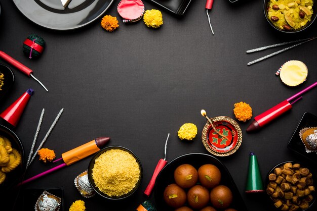 Diwali-snoepjes en snacks gerangschikt in een groep met Diya of olielamp, bloemen en Fire Crackers of Patakhe over humeurig oppervlak, selectieve focus