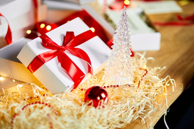 赤いリボンでクリスマスプレゼントの白い箱を包むDIYクリスマスプレゼント、テーブルの上のお祝いの装飾。