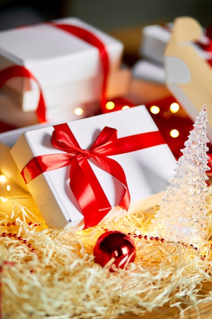 赤いリボンでクリスマスプレゼントの白い箱を包むDIYクリスマスプレゼント、テーブルの上のお祝いの装飾。