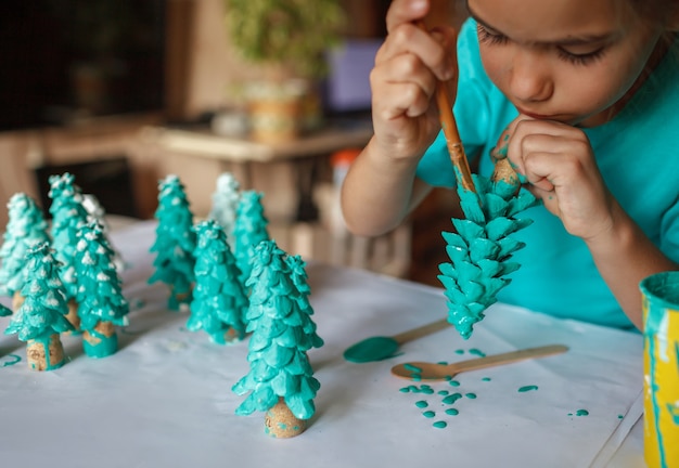 DIY craft gifts and Christmas decoration. Girl coloring cone as if it is pine tree, be green