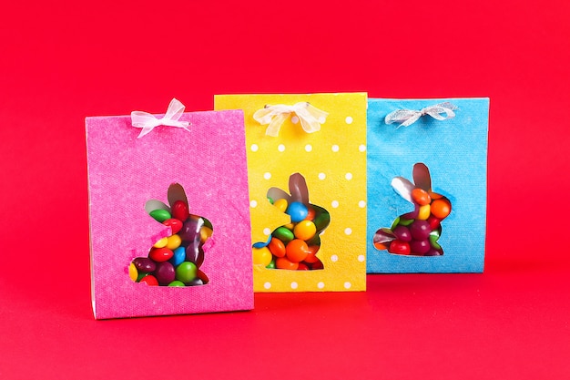 Photo diy easter wrapping package sweets in a bag with a cut out bunny silhouette on a red background.