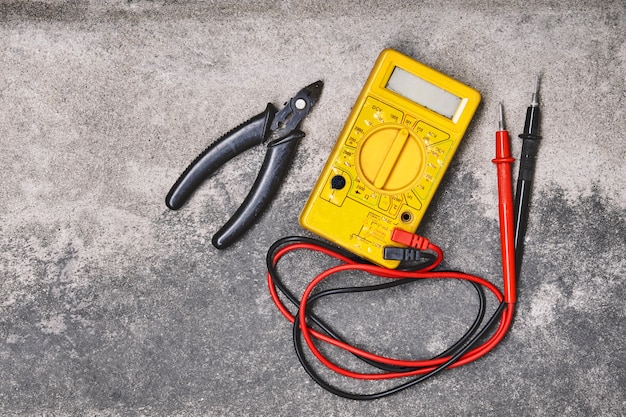 Photo diy home electricity working tools, pliers and yellow multimeter on cement background