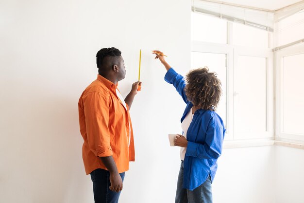 Photo diy home repair black couple with tape ruler measuring wall in room