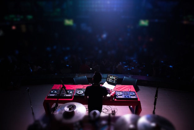 DJ with headphones at night club party under the blue light and people crowd 