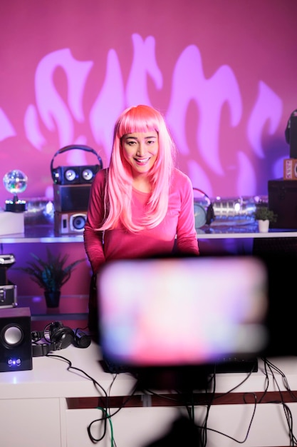 Foto dj con i capelli rosa che esegue canzoni elettroniche su giradischi professionali durante la registrazione di sessioni musicali con la fotocamera, divertendosi in discoteca durante la notte. artista che balla durante l'esecuzione di remix techno