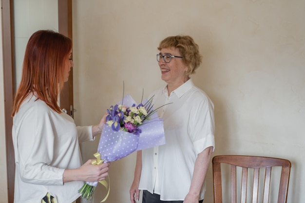 Dochter geeft bloemen aan volwassen moeder Dochter geeft bloemen aan haar moeder en knuffelt haar Tijd samen doorbrengen om thuis te vieren in het weekend Moederdag