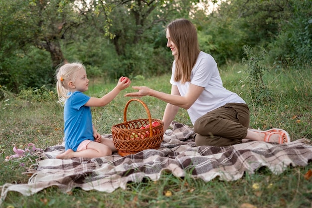 Dochtertje geeft haar appels Jonge moeder op open plek in bos Zomerpicknick van moeder en meisje op geruite deken