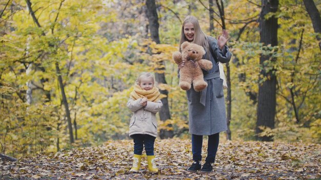 Dochtertje met haar moeder en teddybeer wandelen in herfstpark, telefoto