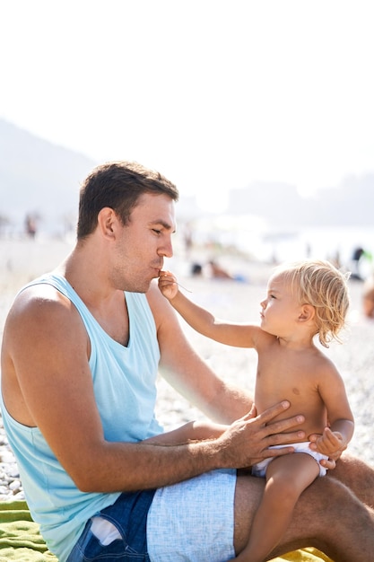 Dochtertje voedt haar vader met de lepel terwijl ze op het strand zit