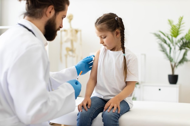 doctor administering vaccine to young girl on medical couch