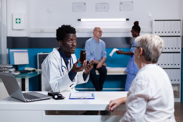 Doctor of african ethnicity holding bottle of pills for old patient