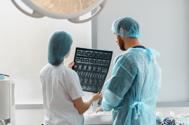 Фото Врач и медсестра в униформе смотрят и обсуждают рентген или мрт позвоночника пациента