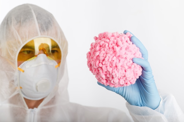 Доктор в противоэпидемическом костюме держит розовый шарик как коронавирус
